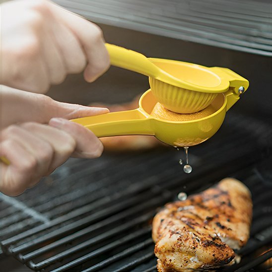 Main pressant un citron avec un presseâagrume manuel auâdessus dâun barbecue.