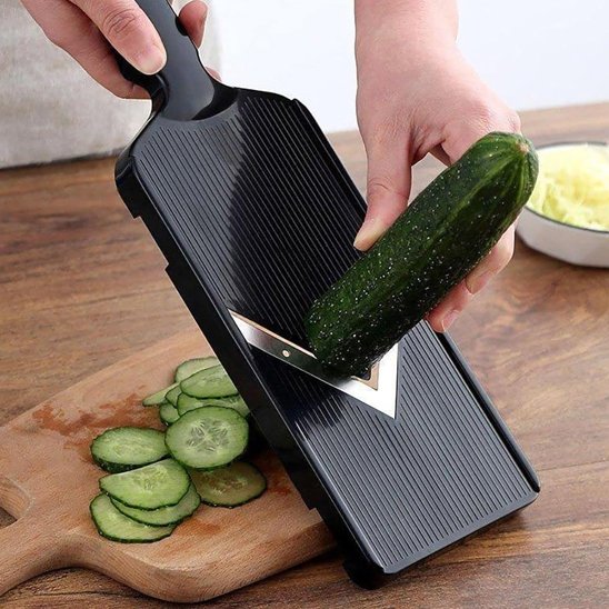 Coupe‑légume manuel noir en action, produisant des lamelles de concombre sur une planche 