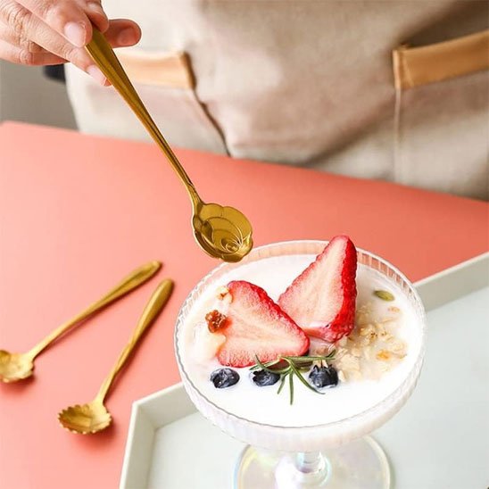 Cuillère à café dorée décorative, utilisée pour remuer une boisson chaude dans une tasse blanche..