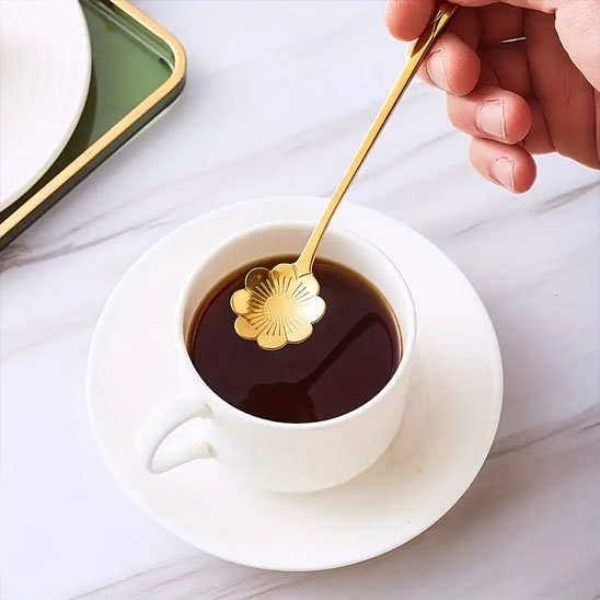 Cuillère à café dorée tenue au‑dessus d’une tasse blanche.