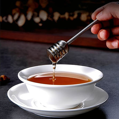 Cuillère à miel métallique tenant du miel au‑dessus d’une boisson chaude.