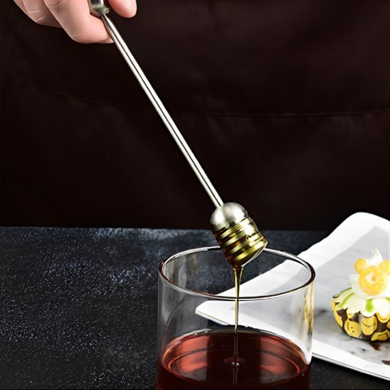 Cuillère à miel métallique utilisée pour sucrer une tasse de thé dans une ambiance chaleureuse.