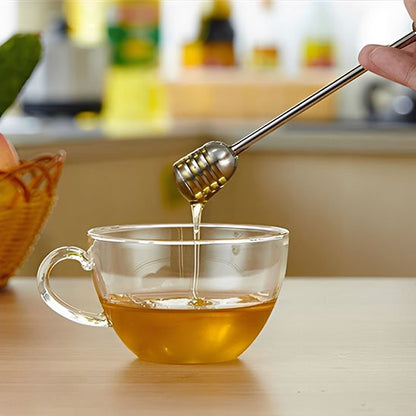 Cuillère à miel métallique versant du miel dans une tasse de boisson chaude.