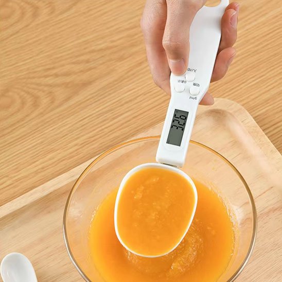 Cuillère doseuse digitale utilisée pour peser du jus d'orange dans un bol en plastique transparent