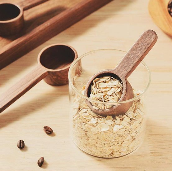 Cuillère doseuse en bois avec café moulu et grains autour.
