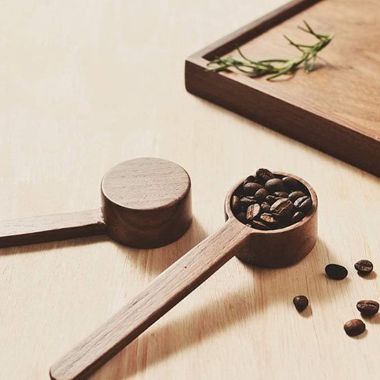 Cuillère doseuse en bois contenant des grains de café.