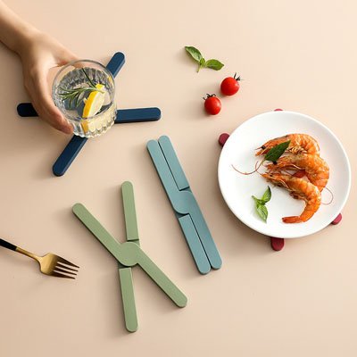 Dessous de plat en silicone vert placé près d'un bol en verre rempli de salade.