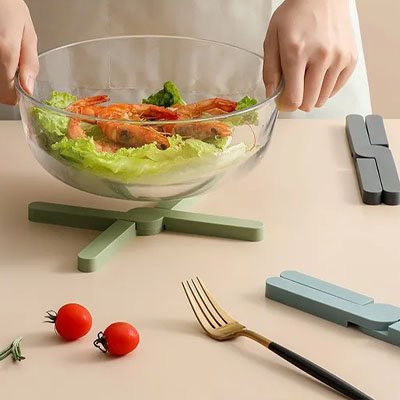 Dessous de plat vert en croix supportant un bol de salade aux crevettes.