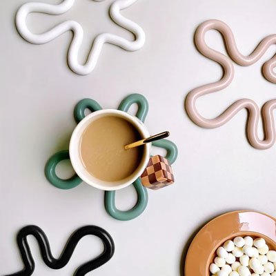 Dessous de plat vert en forme ondulée servant de support à une tasse de café.