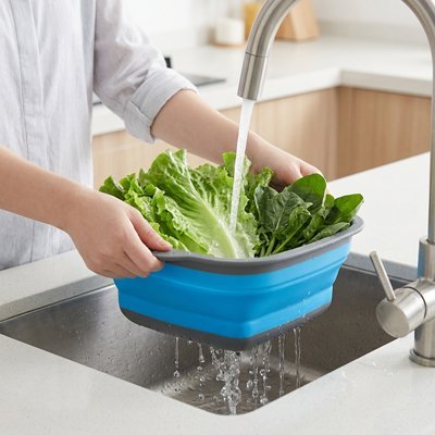  Femme nettoyant des légumes dans une passoire pliable sous le robinet.