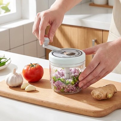 hachoir manuel avec manivelle pour hacher légumes, ail et oignons rapidement, démonstration en cuisine sur planche en bois.