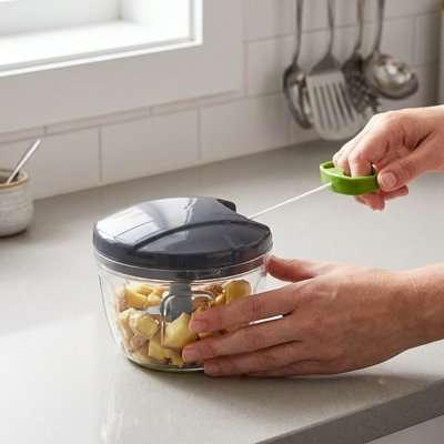 Hachoir manuel utilisé pour couper des aliments dans un récipient transparent