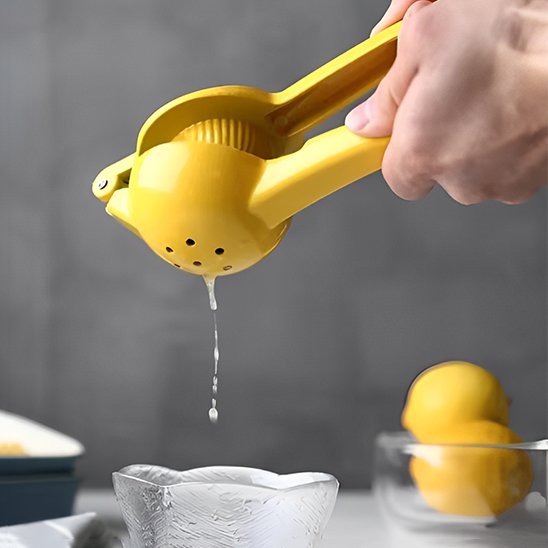 Main pressant un citron avec un presse‑agrume manuel au‑dessus d’un verre dans une cuisine.