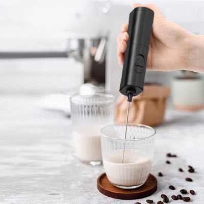 Main utilisant un mousseur à lait pour préparer une mousse épaisse.