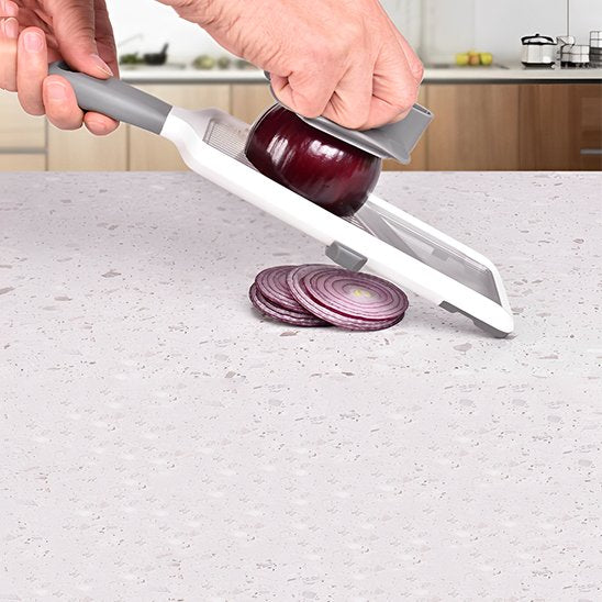 Mandoline avec lame diagonale, coupant un oignon en rondelles.