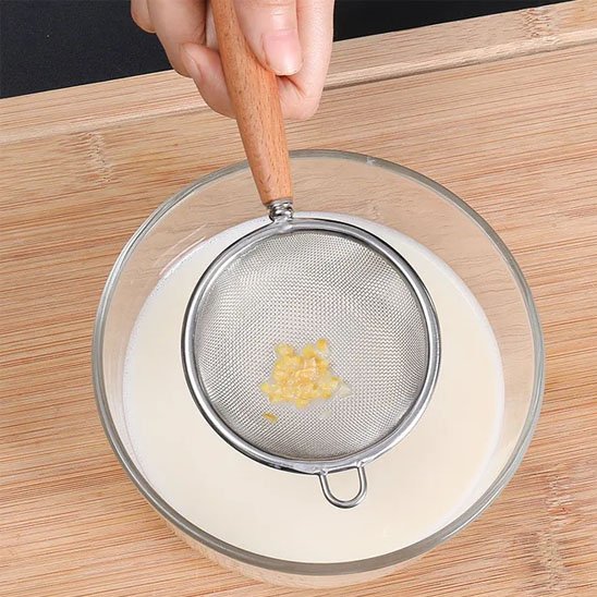Passoire à maille fine avec manche en bois filtrant un liquide dans un bol transparent.
