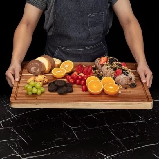 Personne tenant une planche en bois chargée de fruits et pâtisseries.