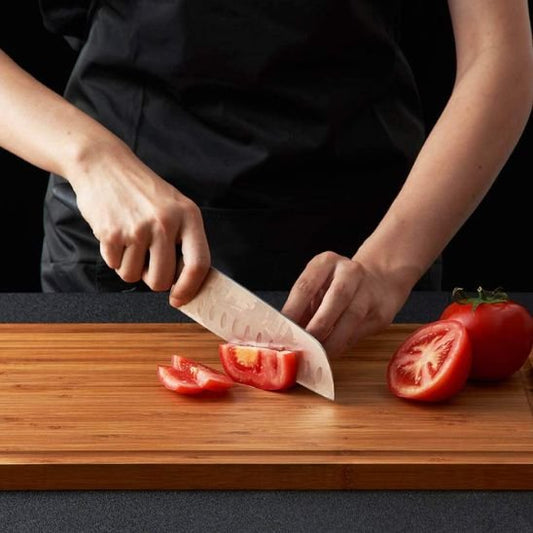 Planche à découper en bois utilisée pour trancher une tomate fraîche.