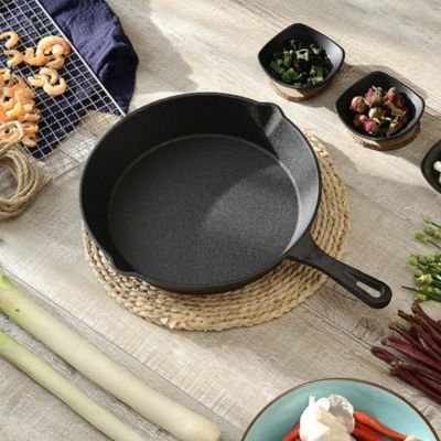 Poêle en fonte présentée avec ingrédients variés pour future préparation culinaire. 