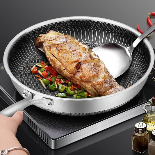 Poêle inox antiadhésive contenant un poisson cuit avec légumes colorés sur plaque à induction.