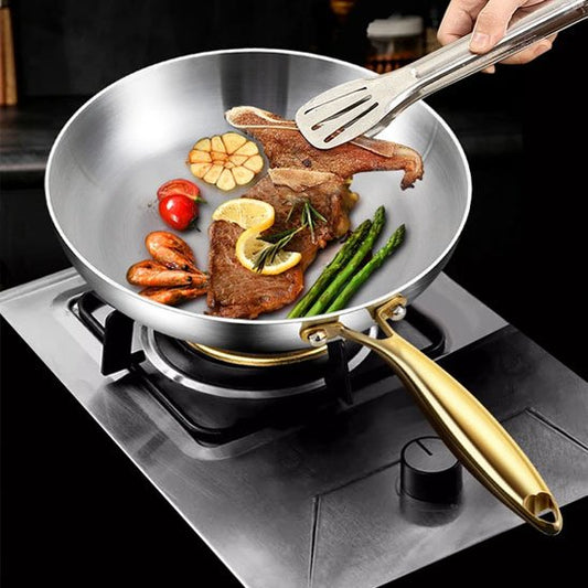 Poele inox chauffée sur un feu à gaz, contenant viande, crevettes et légumes en cuisson.