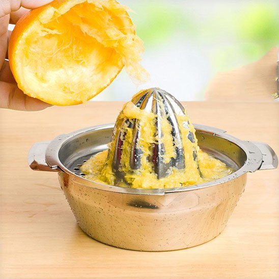 Presse agrumes en inox utilisé pour extraire du jus d’orange sur un plan clair.