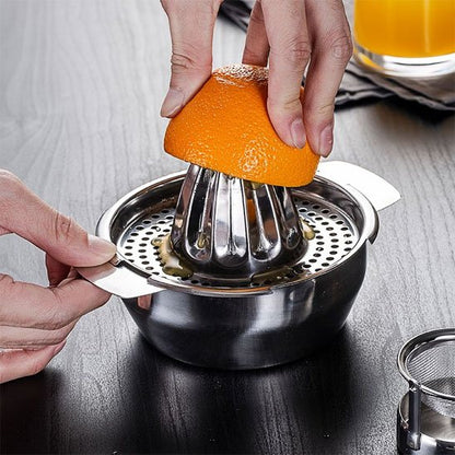 Presse agrumes manuel en acier avec pulpe filtrée et oranges coupées en arrière‑plan.