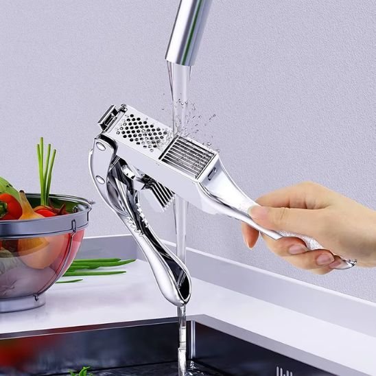 Presse‑ail en inox écrasant de l’ail frais au‑dessus d’une assiette.