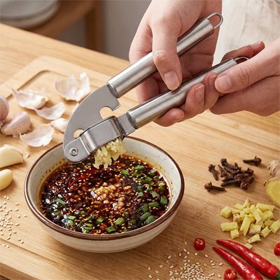 Presse‑ail en inox écrasant de l’ail frais dans une sauce aromatique.