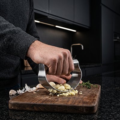 Presse‑ail en inox manipulé pour hacher de l’ail sur une planche de préparation.