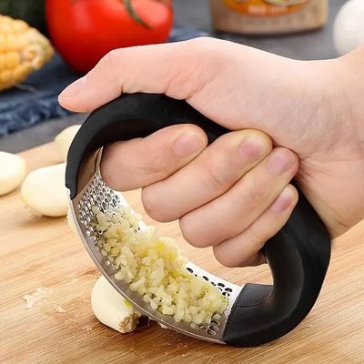 Presse‑ail en inox placé sur une planche près d’ingrédients frais.