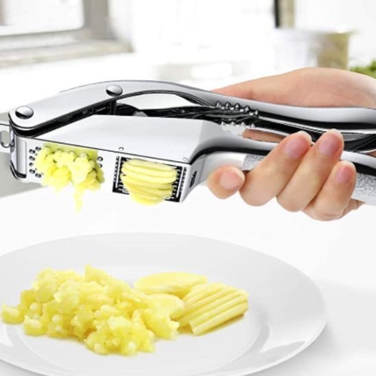 Presse‑ail métallique extrayant de l’ail finement écrasé sur une assiette blanche.