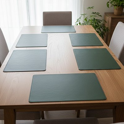 Set de table vert sur une grande table en bois, avec lumière naturelle et plante décorative en arrière‑plan.