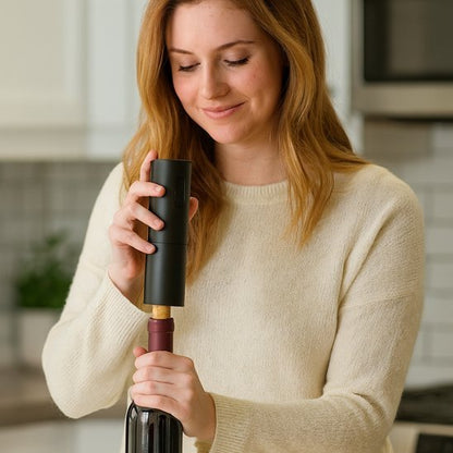 Tire bouchon électrique débouchant une bouteille de vin posée sur une table en bois.